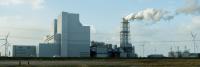 A power plant with wind mills and a smoke column in the center. 